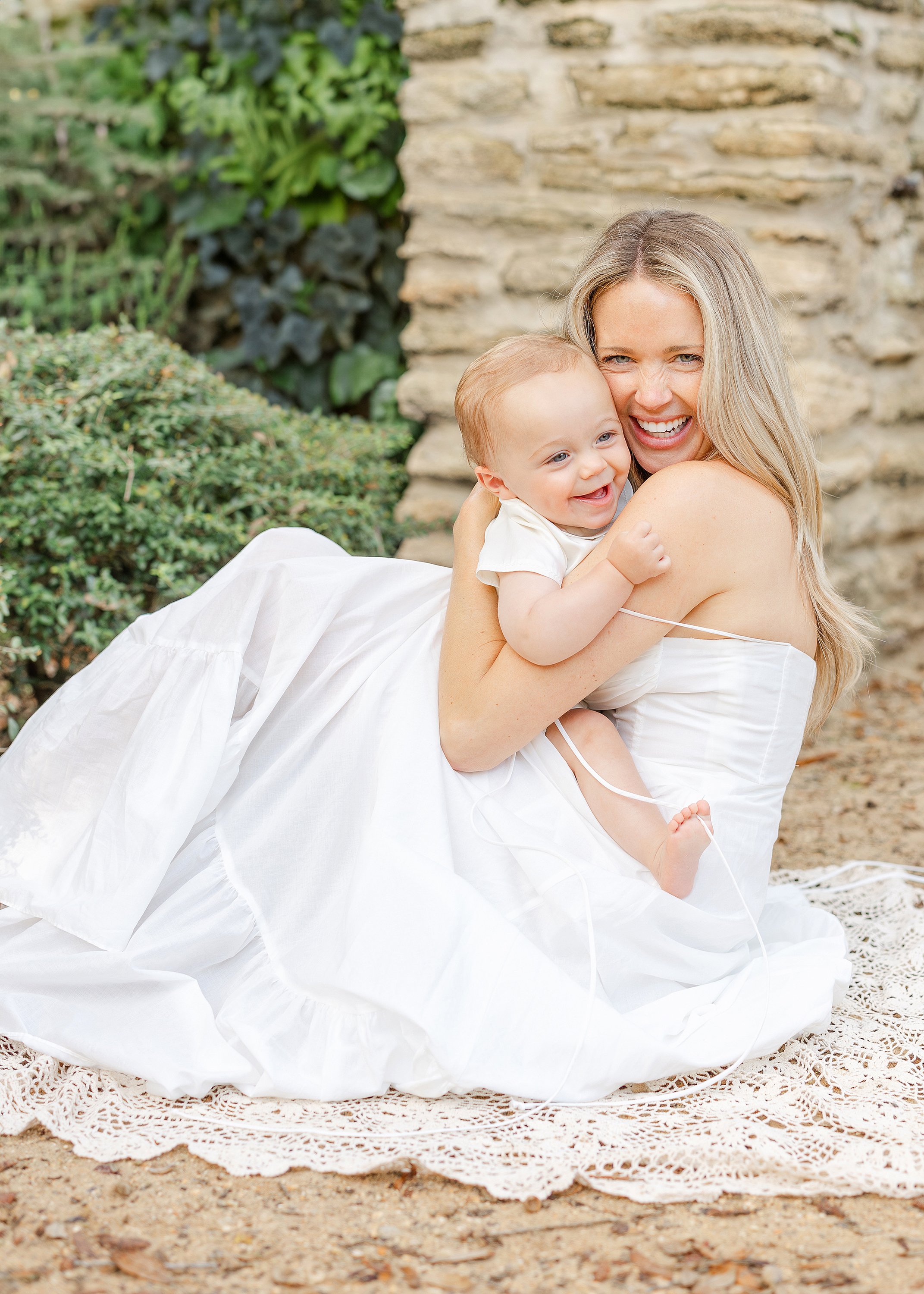 An airy springtime portrait of a mother in a white dress holding her baby boy.