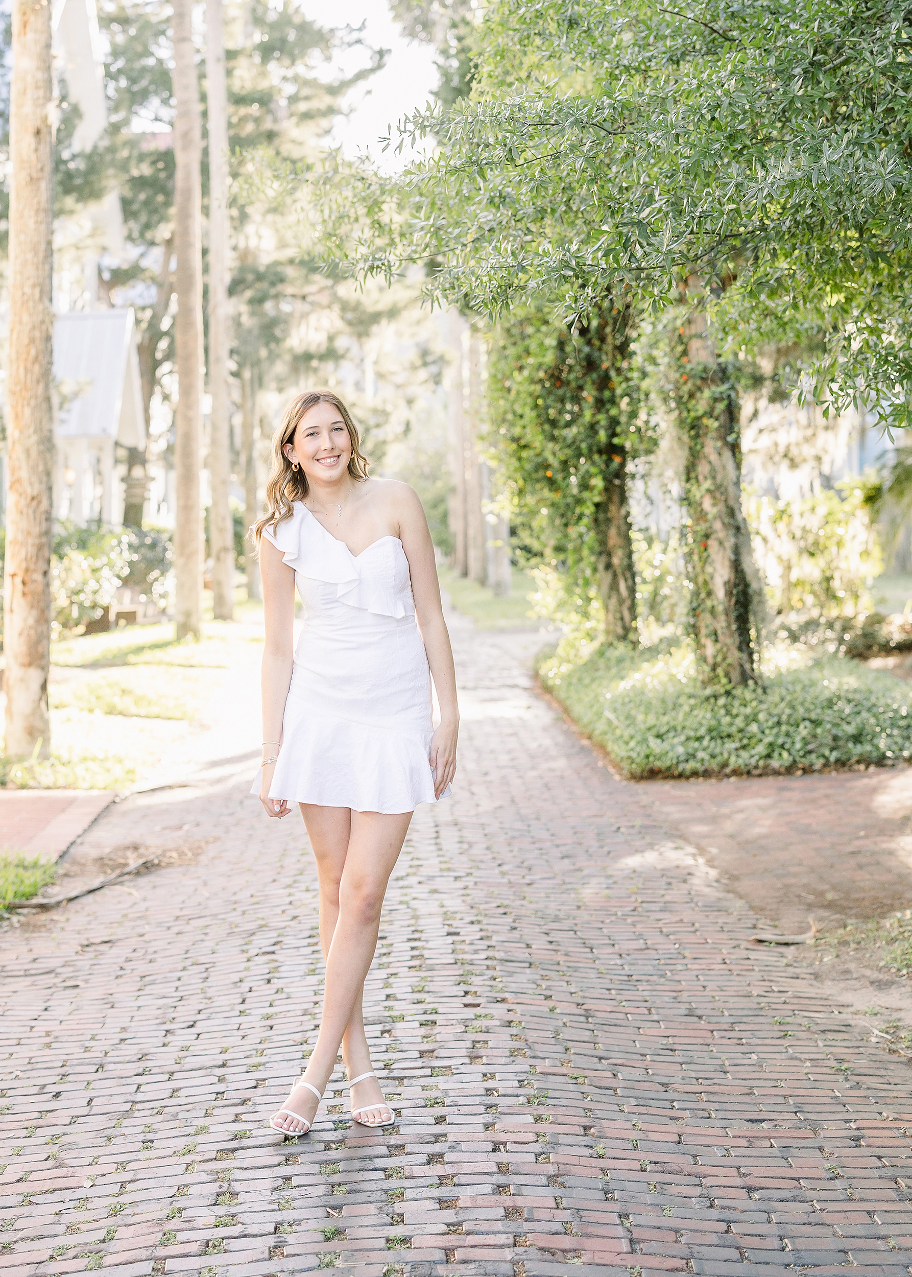 Portrait of a young woman in white dress and white heels standing on a brick road in downtown St. Augustine, Florida.