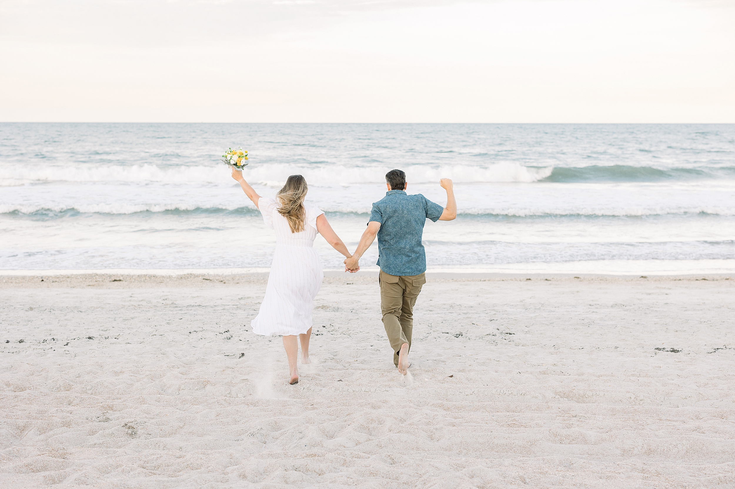 A couple runs towards the ocean at sunset in St. Augustine Beach, Florida.