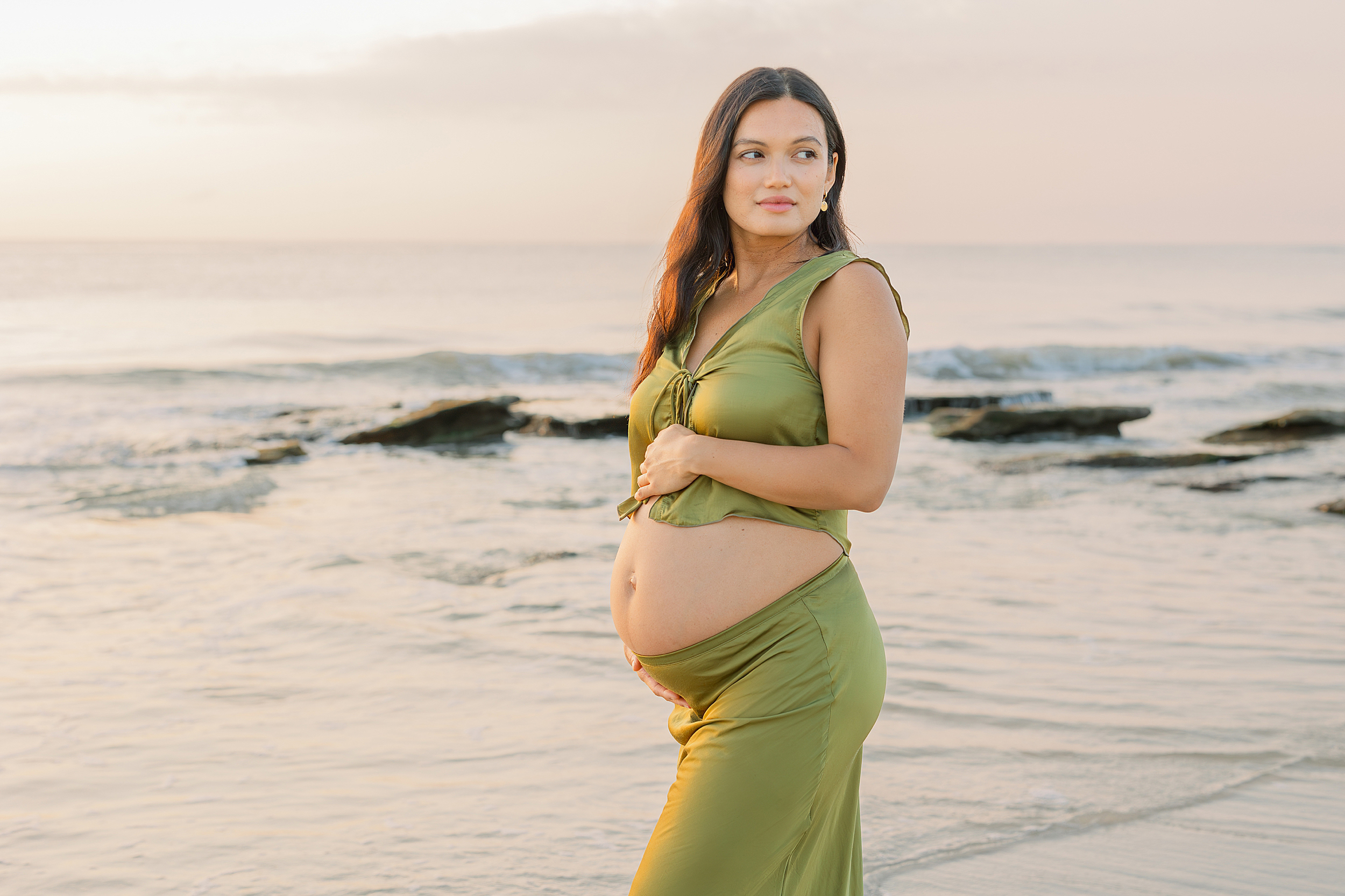 A sunrise maternity portrait of a woman in green satin on the beach.