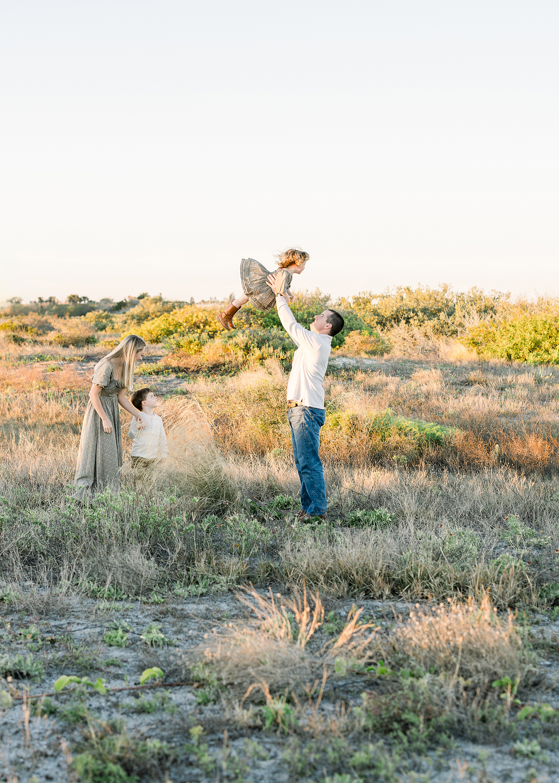 A father throws his little boy in the air at sunset on the sand dunes at the beach.