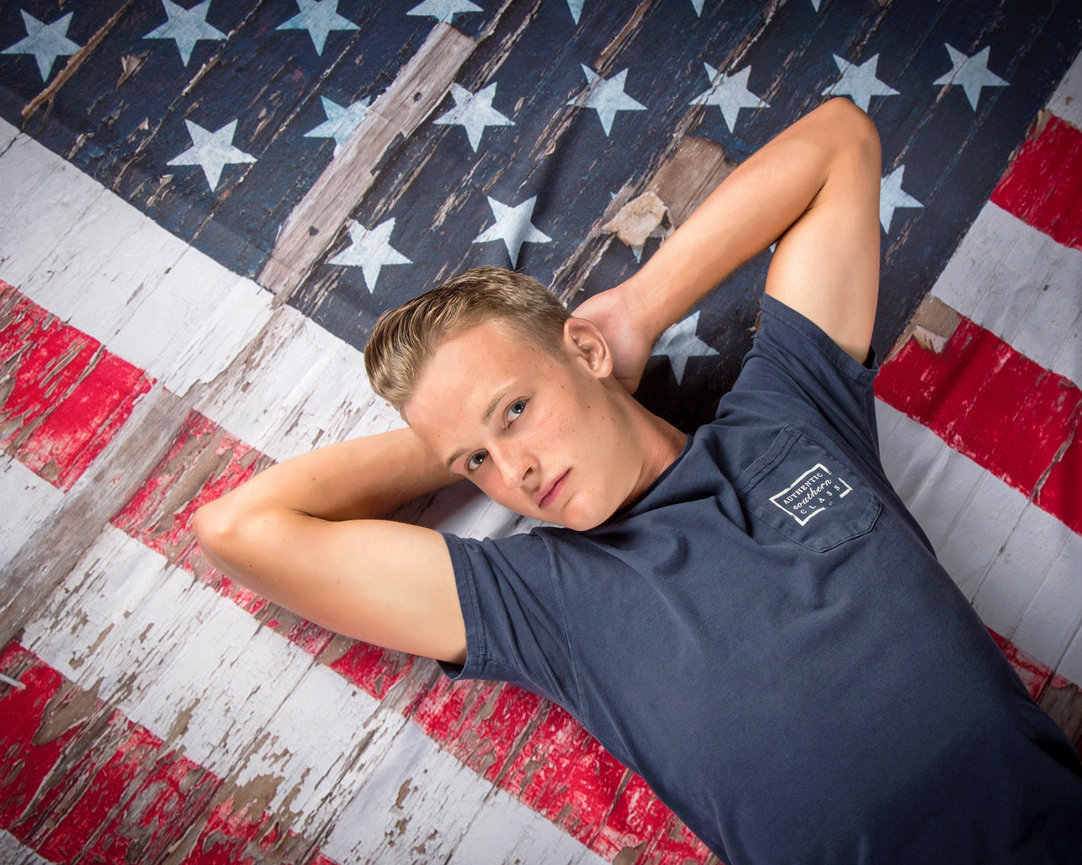 Person lying on a US flag-themed background, wearing a dark t-shirt, gazing upwards.