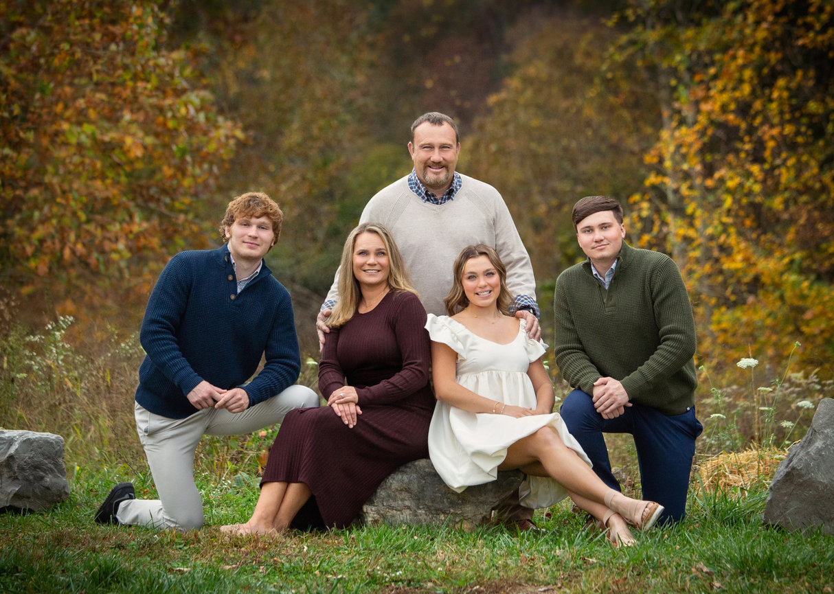 A family of five poses outdoors with fall foliage in the background.