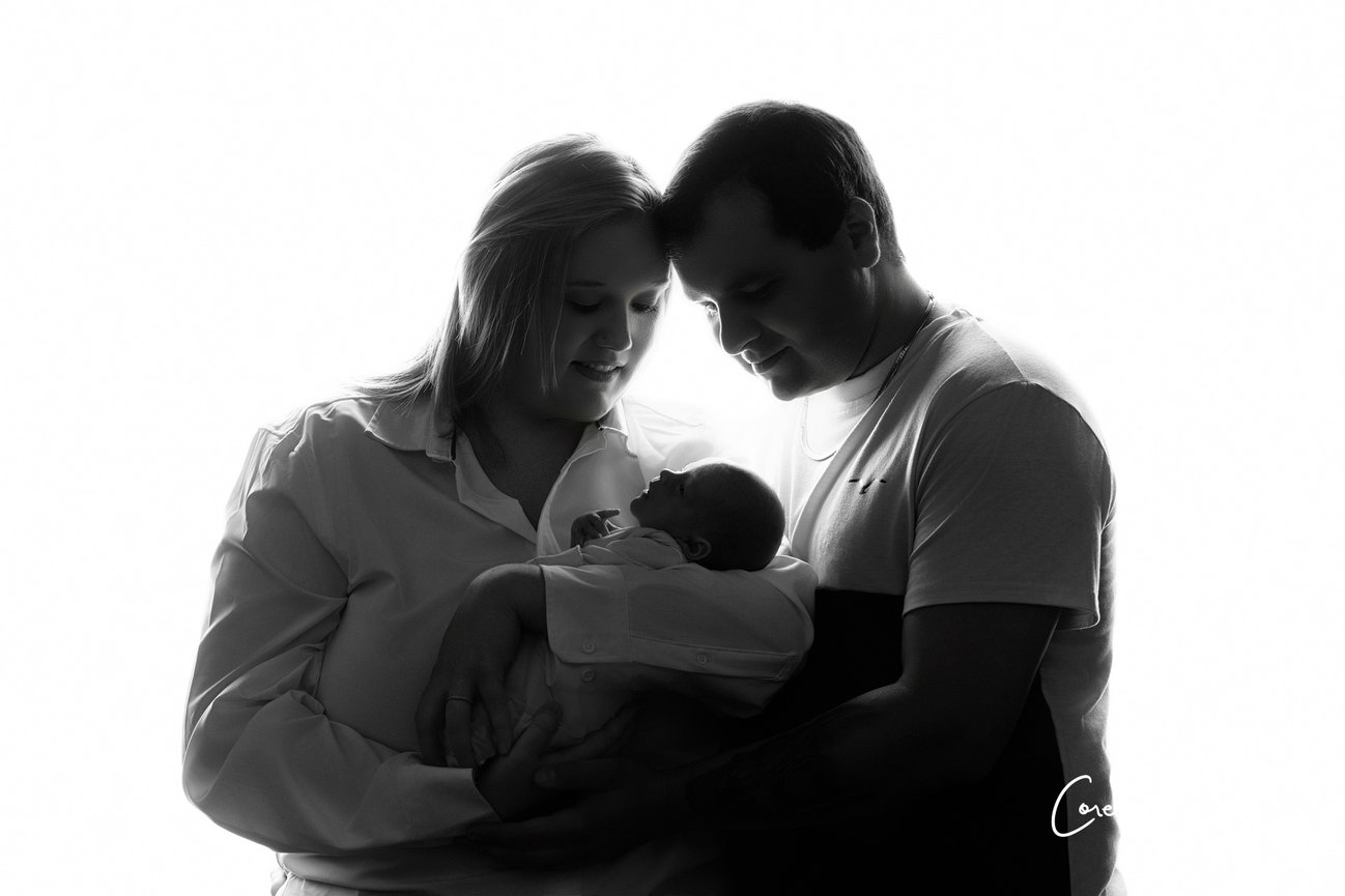 Silhouetted couple lovingly holding a baby against a white background.