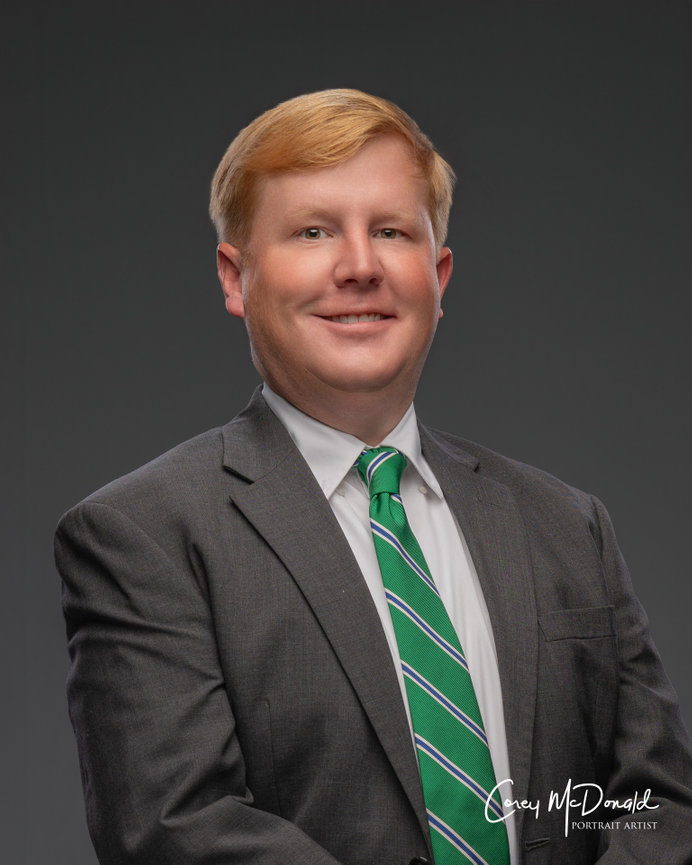 Man in a suit with a green striped tie against a dark gray background.