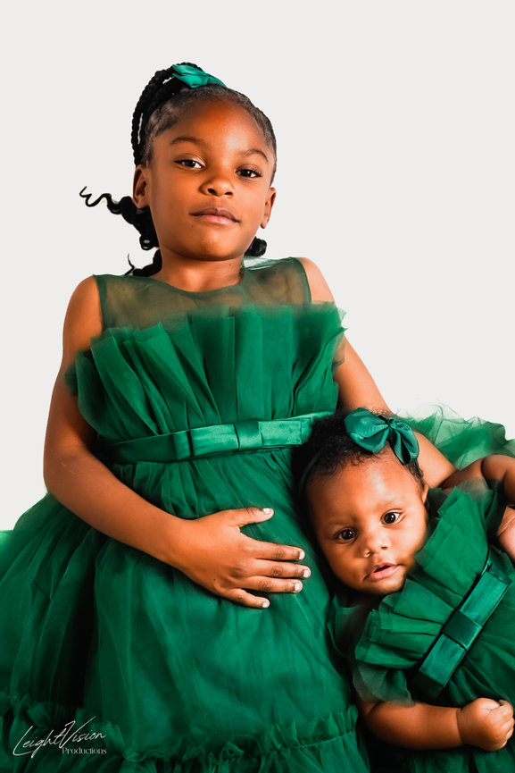 Two young girls wearing matching green dresses and shoes, smiling and enjoying a sunny day outdoors.