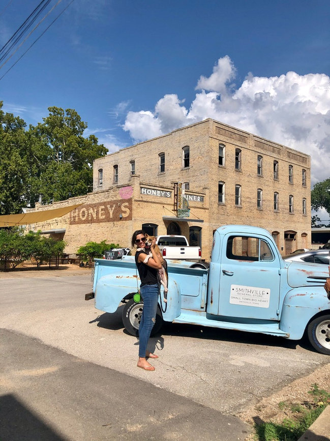 Woman posing beside a light blue vintage truck on a sunny street.