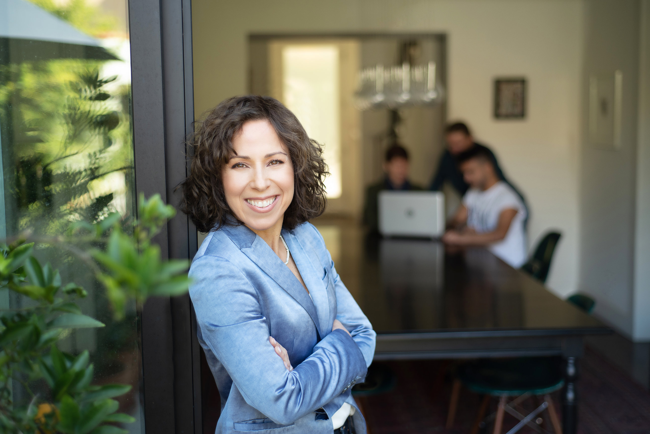 Female business owner in blue velvet jacket with team working in background