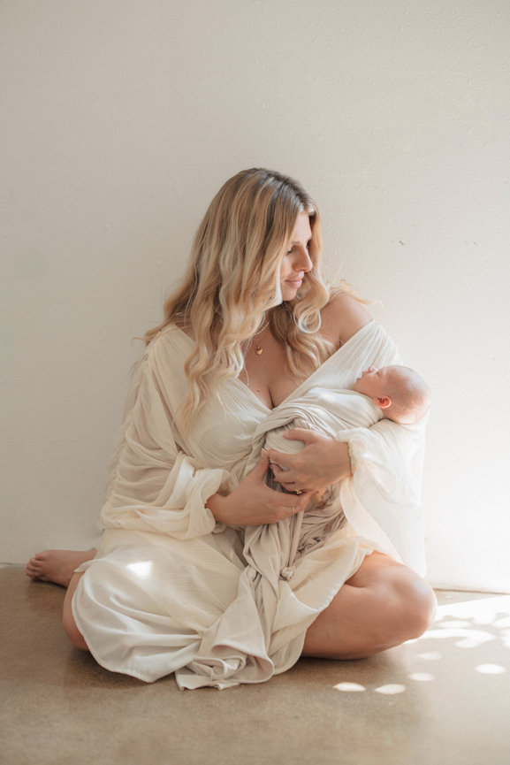 Orange County Mother holding a baby in a soft natural light setting, wearing a flowing cream