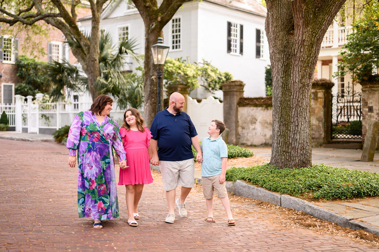 family of four holding hands walking down a brick street wearing spring colored ourfits
