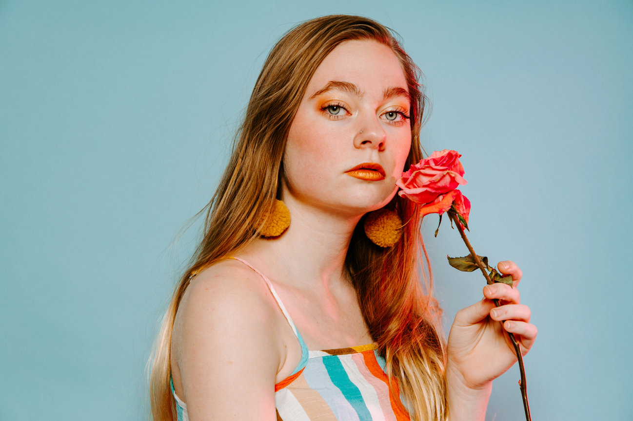 Woman holding rose in front of pastel background