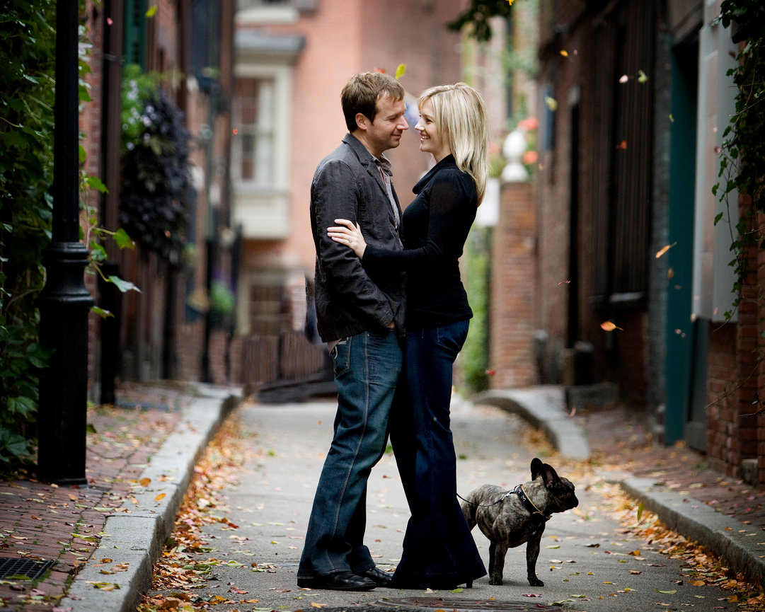 Couple standing together on a cobblestone alley with a small dog beside them