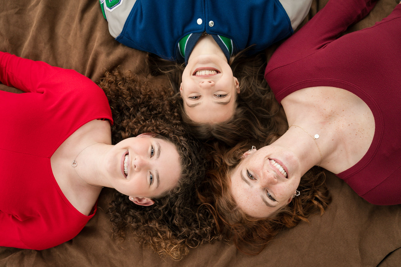 Three senior girls on the Case Studios Photography senior team lying on a brown surface, heads together, smiling in Lee's Summit, MO