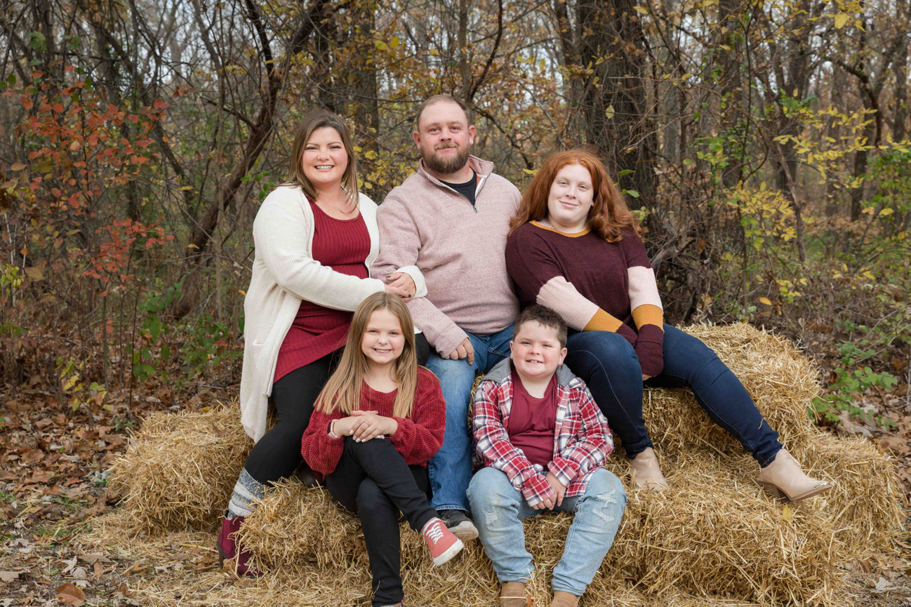 Family of five posing on hay bales in an autumn forest setting in Blue Springs, MO photographed by Case Studios Photography
