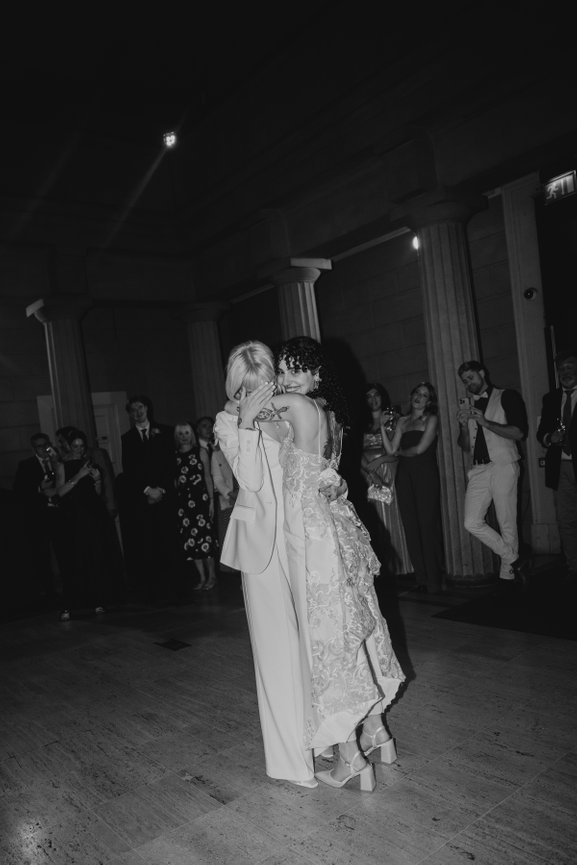 Direct flash photography of two brides during first dance at Manchester Art gallery with guests watching.