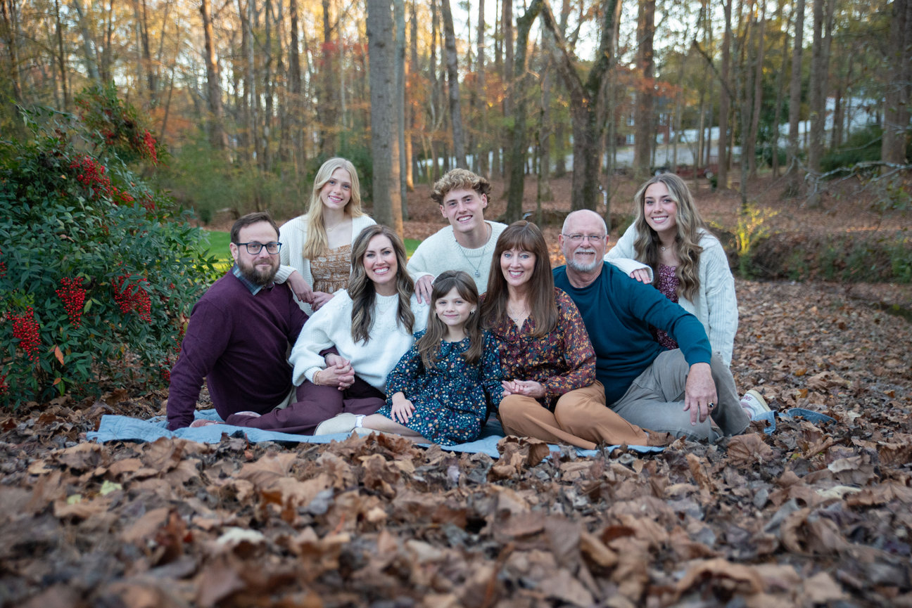 Family lying together on fallen leaves in a forest.