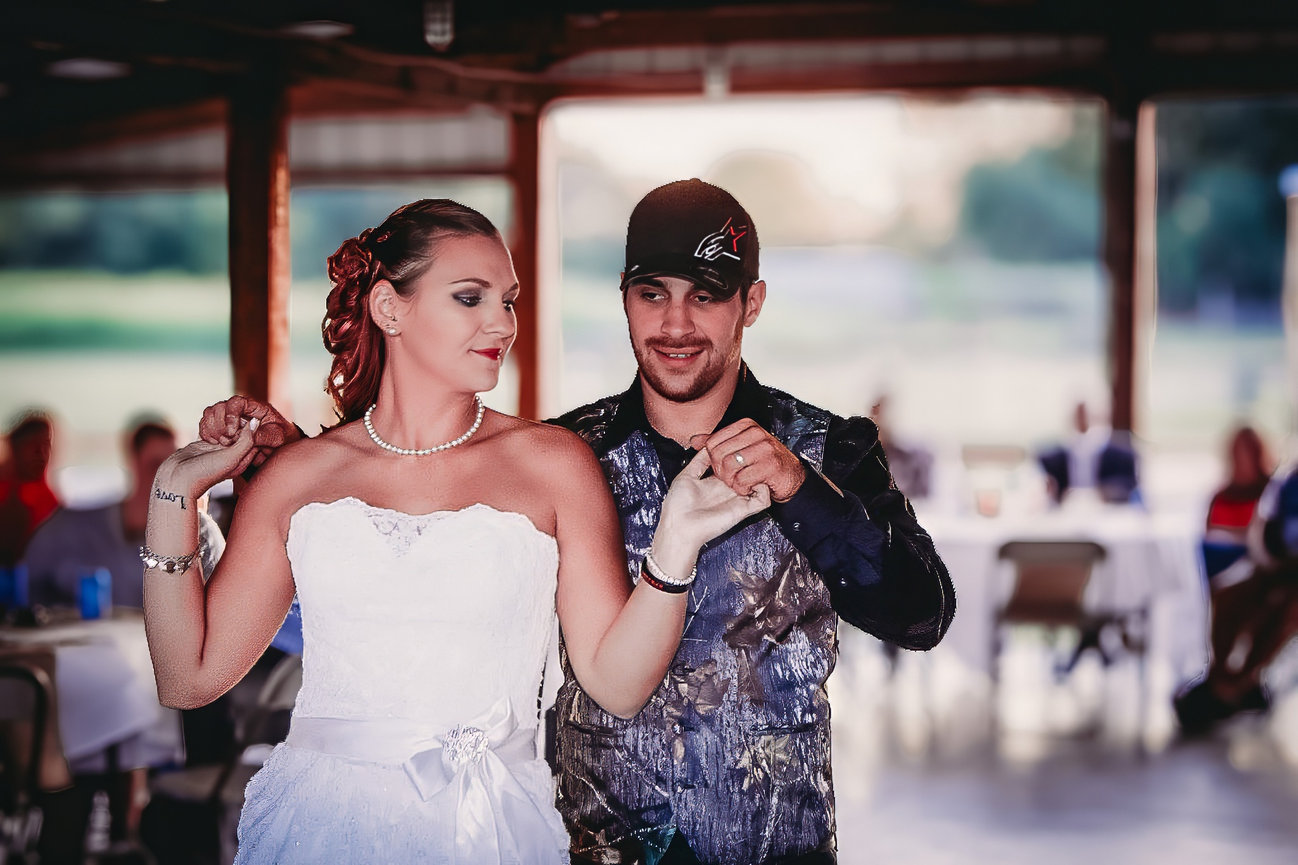 A bride and groom dance together in a reception venue, wearing casual attire.
