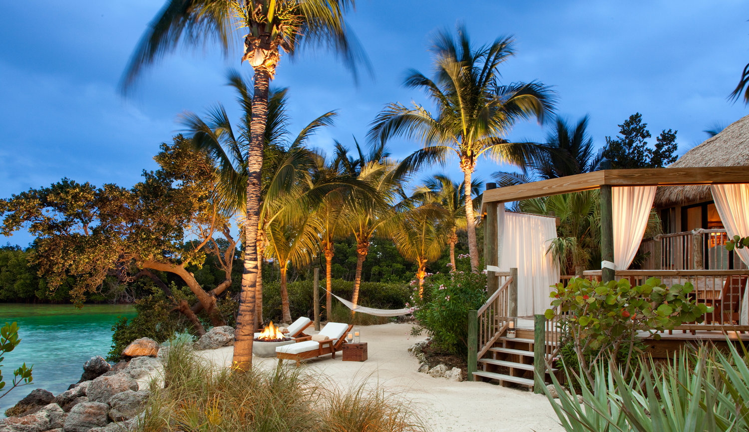 Little Palm Island Suite with Large Balcony and lounge chairs set up by fire on the ocean on a perfect evening.