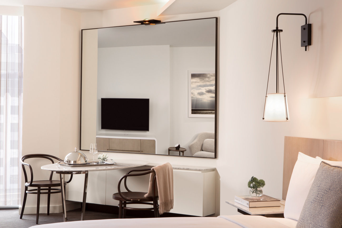 Guest Room sitting area at the Conrad DC showcasing a large Mirror reflecting a spacious Guest room along with beautiful lighting fixtures ad a 5 star Breakfast setup at table.