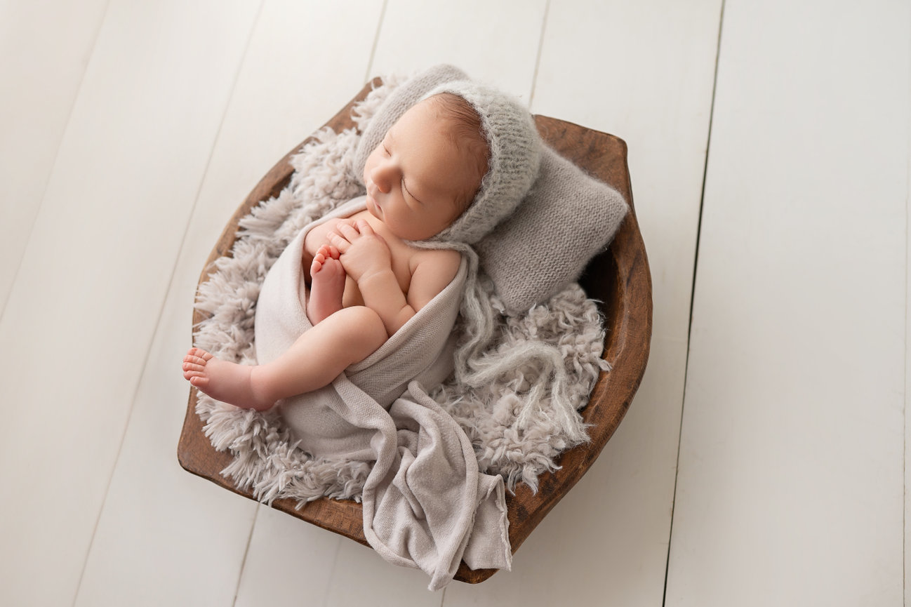 Newborn curled up in wooden bowl with neutral layers, captured in NJ photography studio