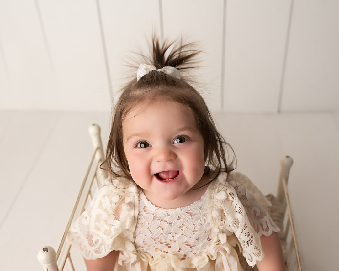 Timeless birthday photo of baby on white wrought iron ned against clean backdrop in Toms River, NJ