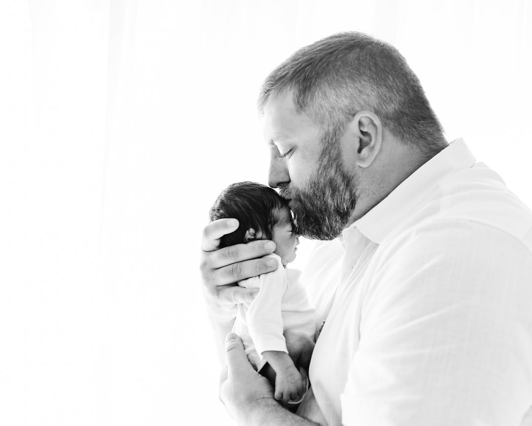 Emotional black and white portrait of dad cradling baby against white backdrop in Monmouth County studio