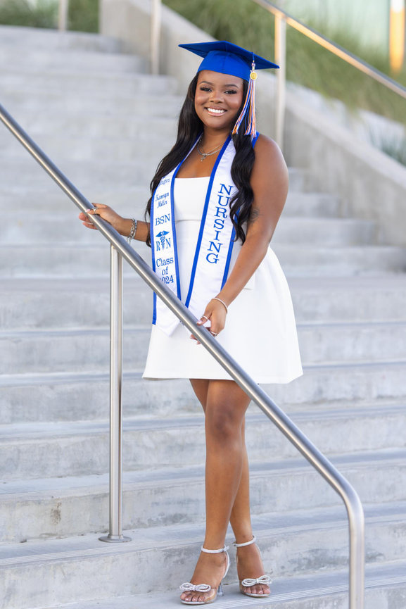 Graduating student in a white dress and cap, proudly holding nursing sash on stairs at the University of Texas at Arlington