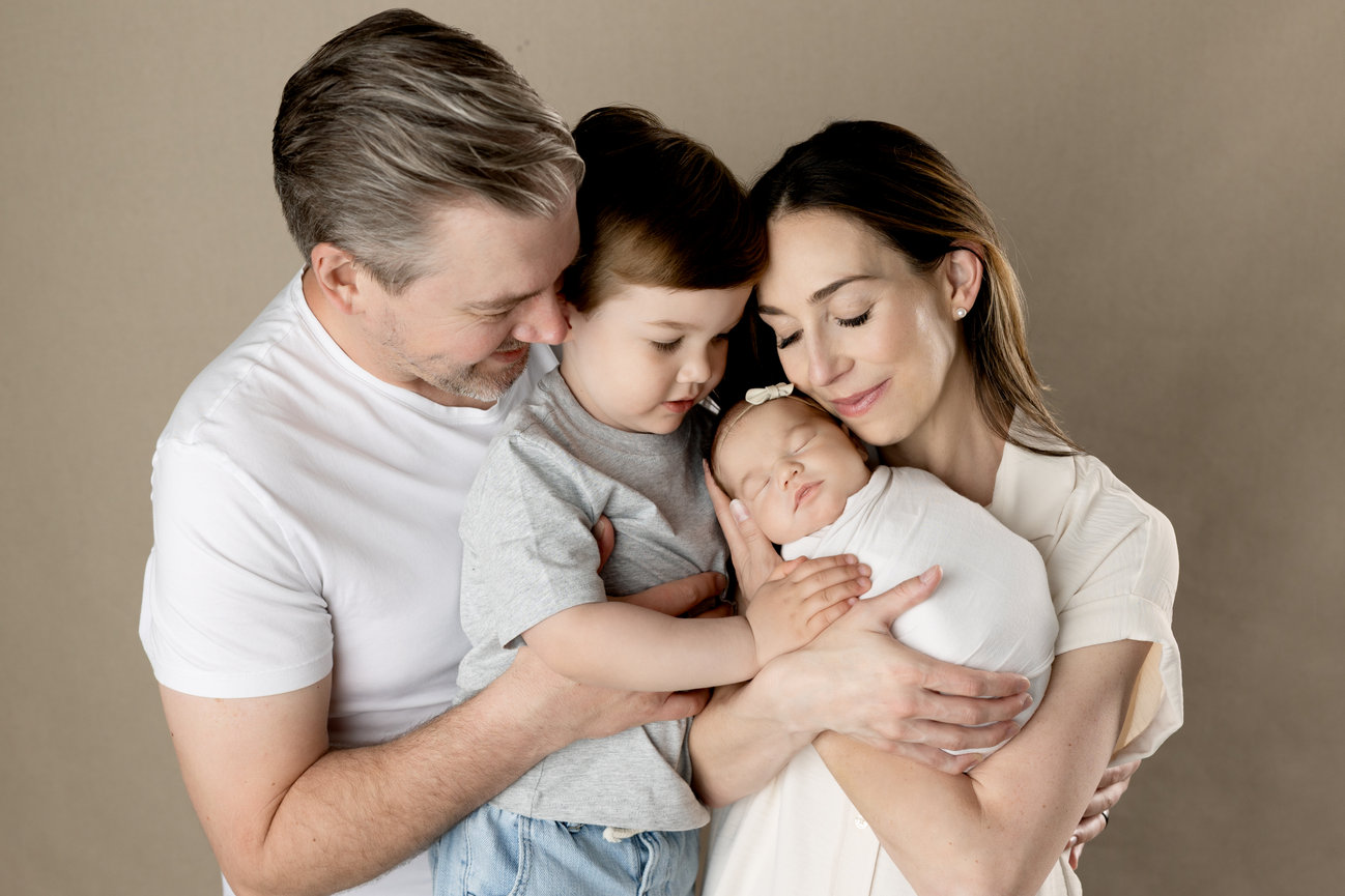 A family with a couple holding a toddler and a sleeping baby in their arms, all showing affection.