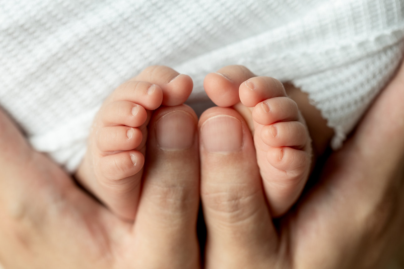 Close-up of adult hands cradling a baby's feet in a tender gesture.