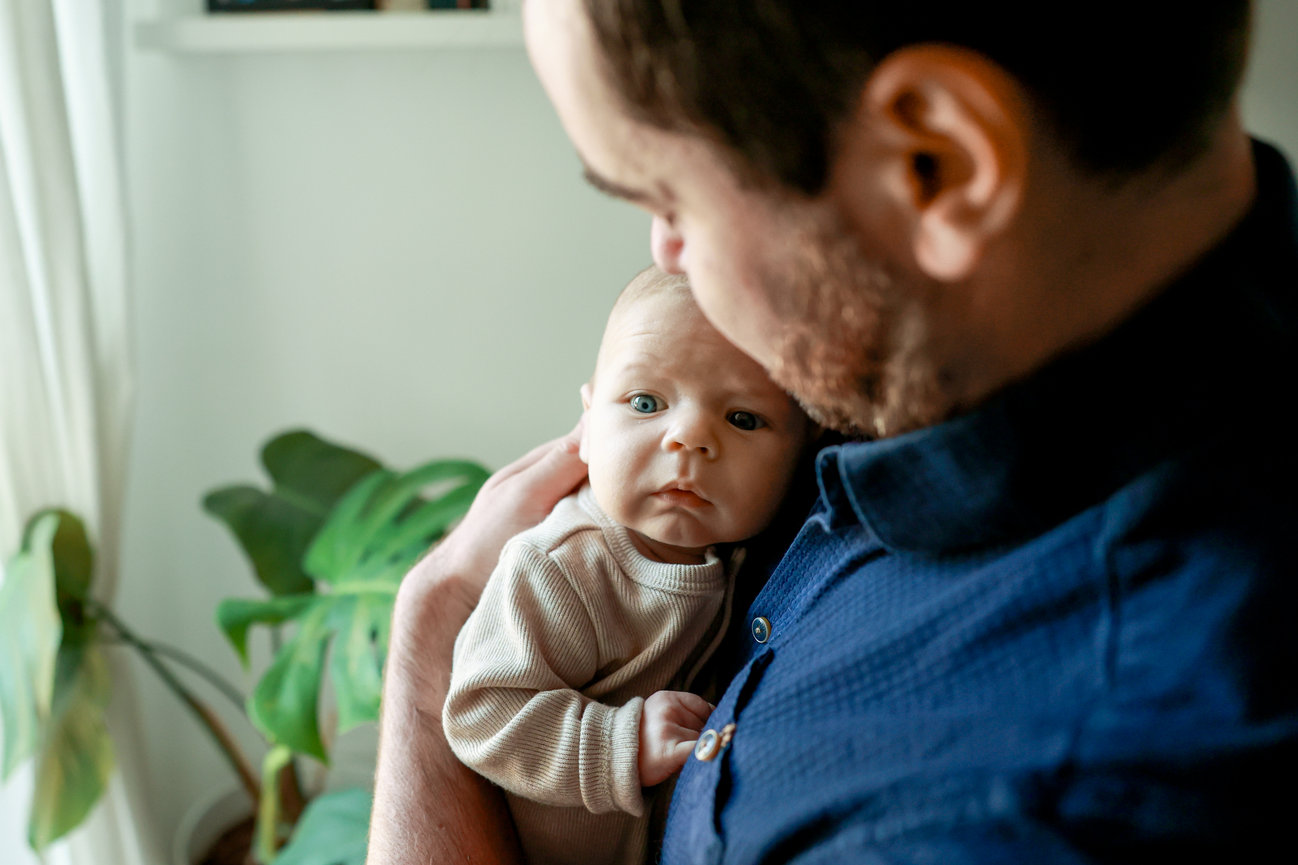A person holding a baby in a cozy room with a plant in the background.