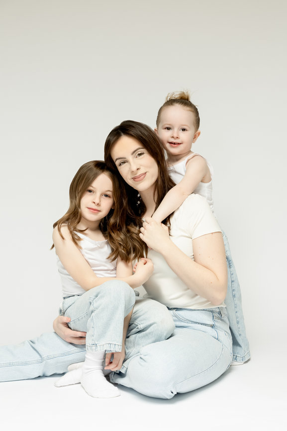 Mother with two young daughters posing in a white studio, wearing matching light clothes