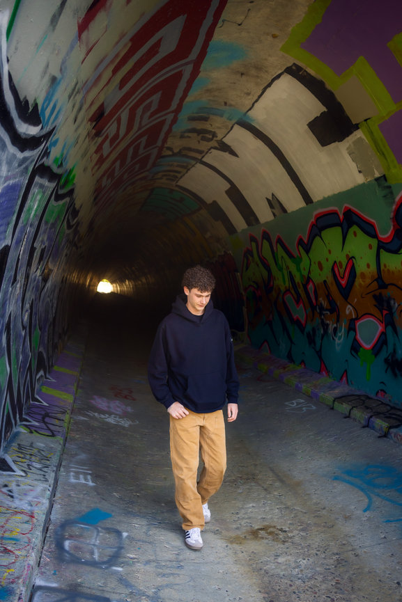 Young man walking through a graffiti covered tunnel in a dark hoodie and tan pants