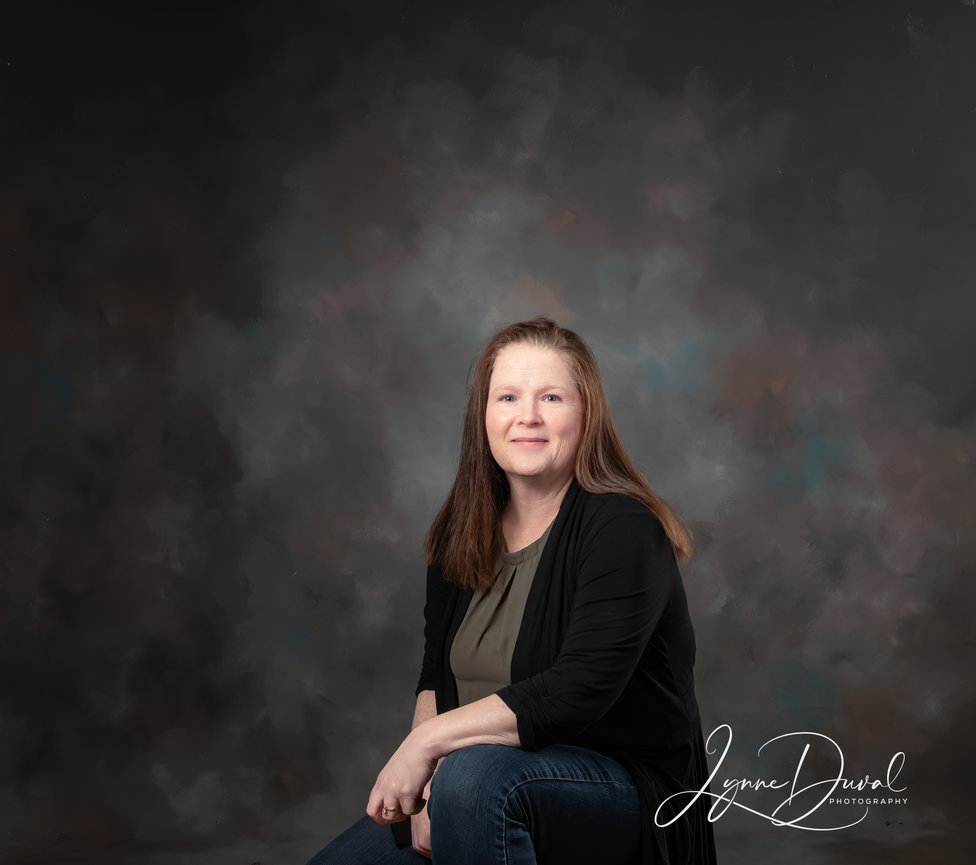 Red haired woman sitting down wearing jeans, black cardigan and green shirt looking at the camera
