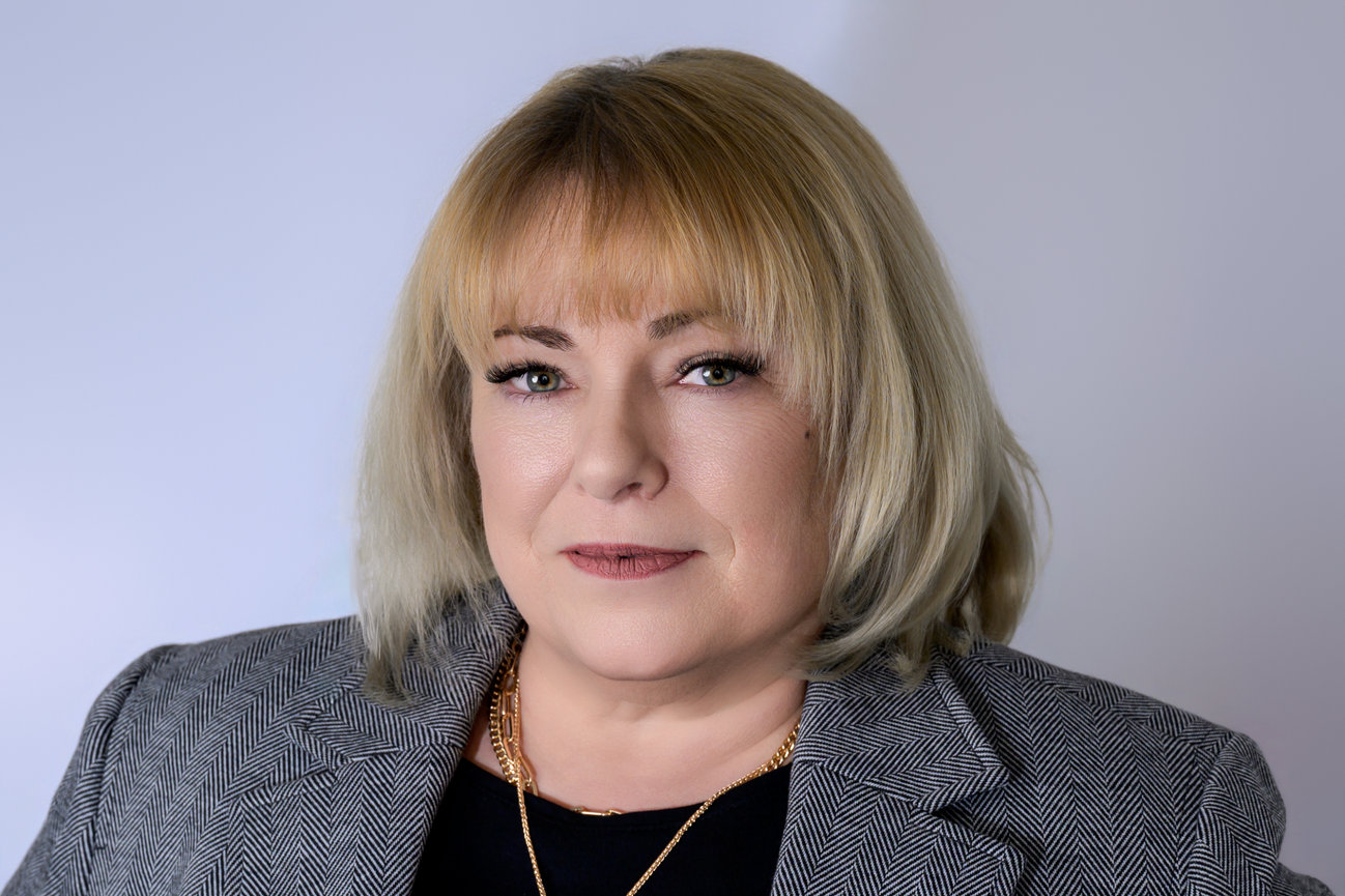 headshot of woman in grey blazer looking straight at camera with blonde hair