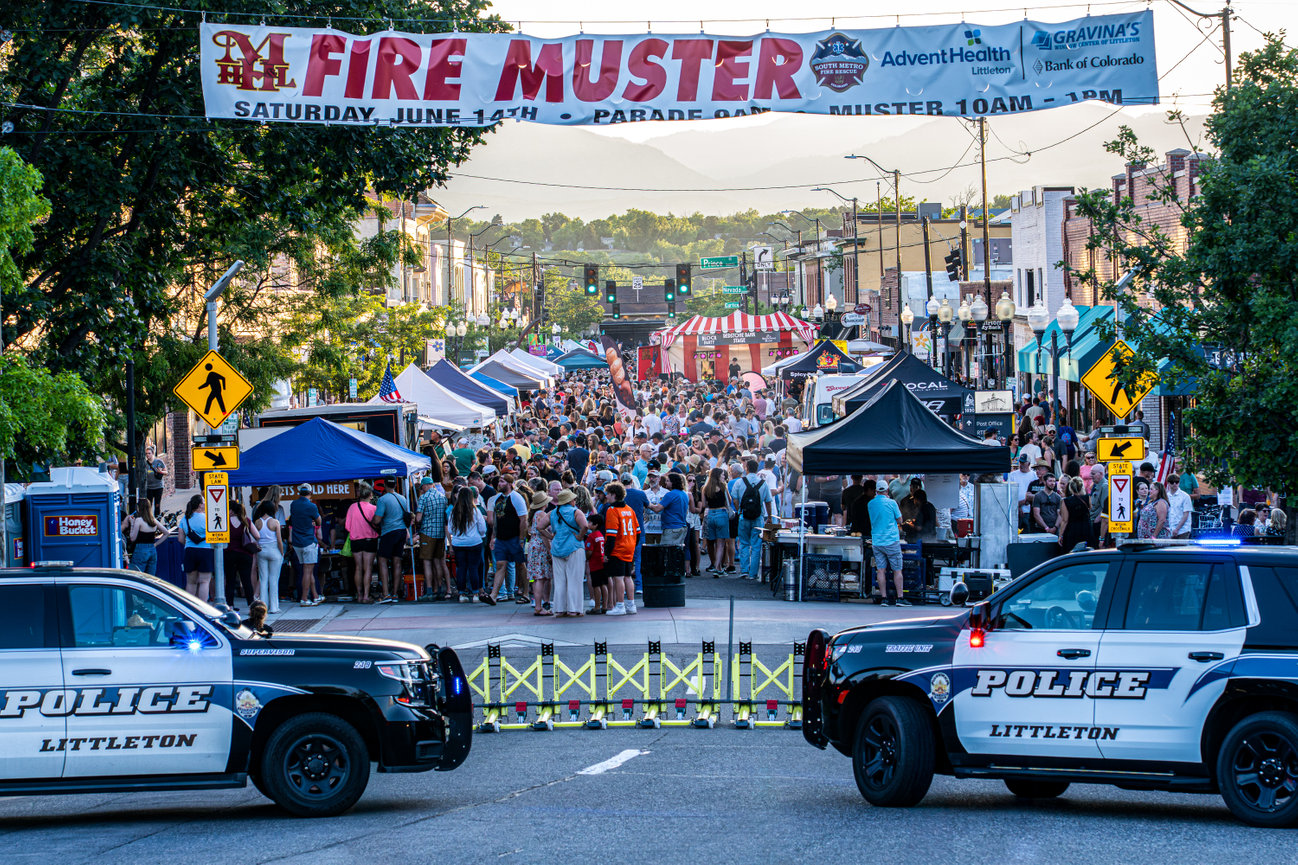 Fire muster parade with emergency vehicles, banners, and a crowd lining the street.