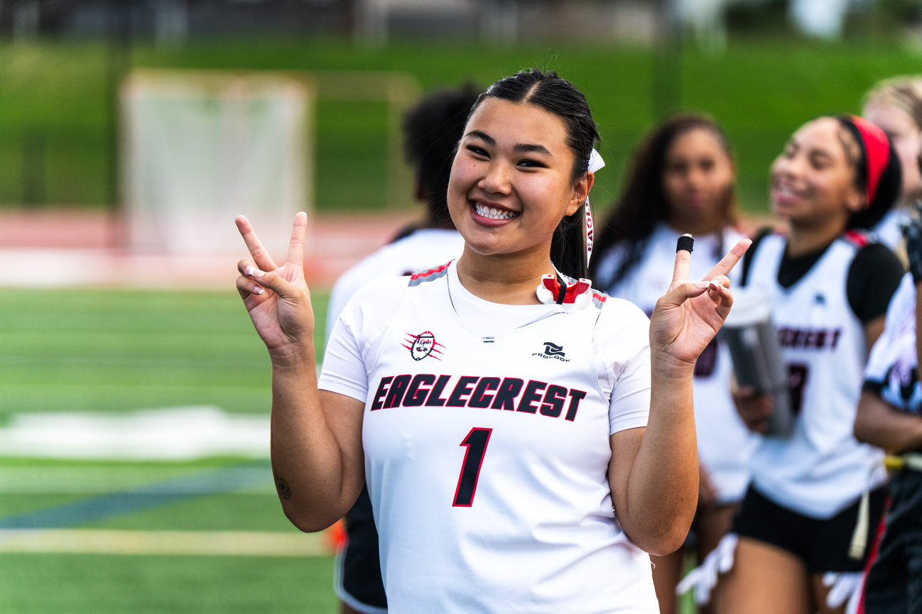 Smiling female athlete on a football field making a peace sign.