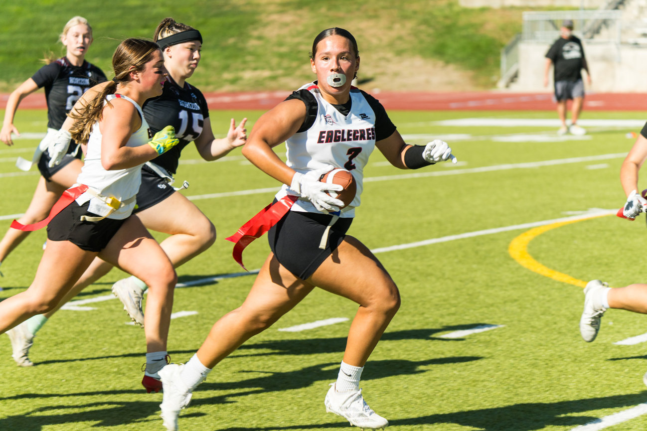 Girls flag football players sprinting down the field during a game.