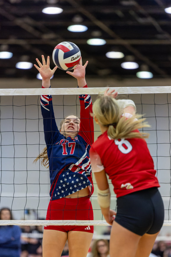 Two volleyball players reaching for the ball at the net.
