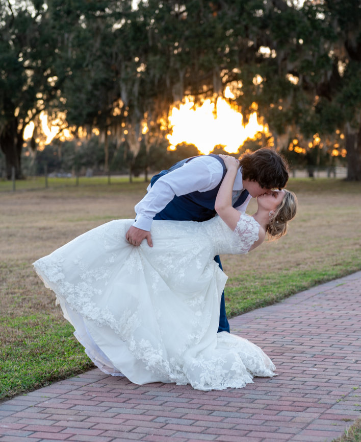 Groom lifting and kissing the bride at sunset in a grassy field.