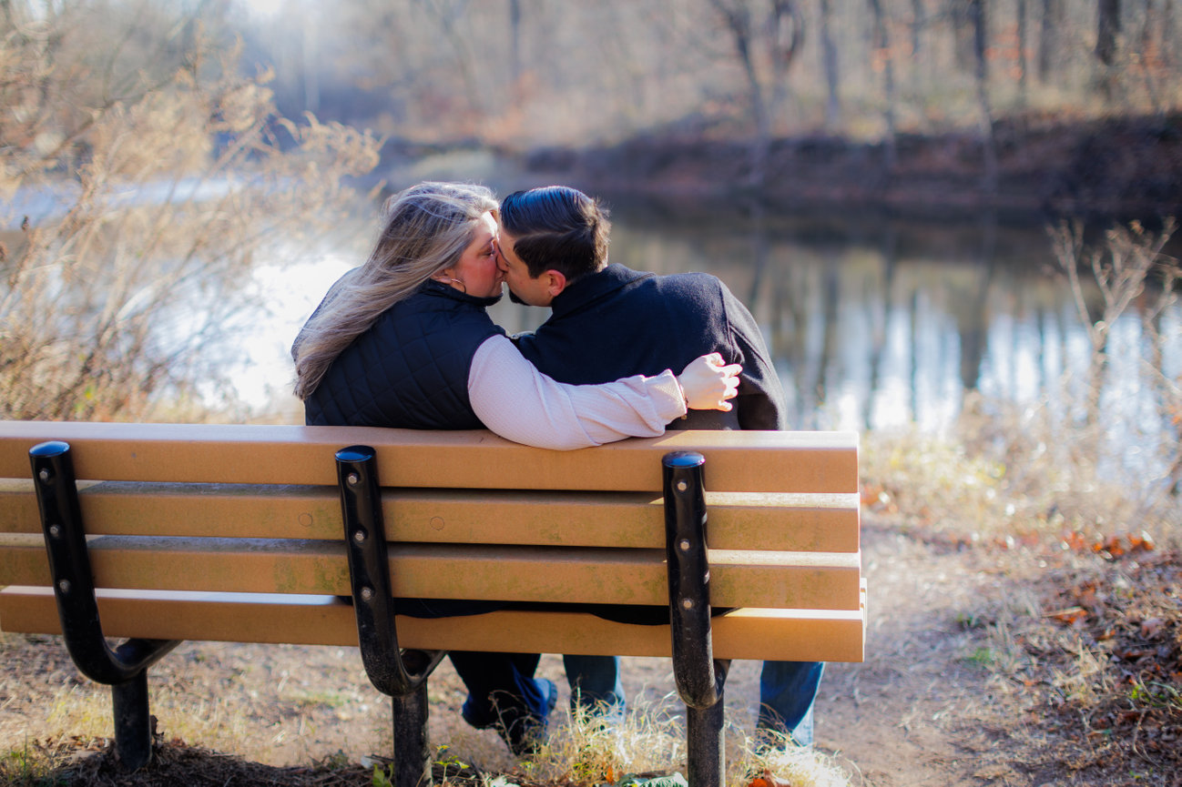 Couple kissing on a park bench beside the water during an engagement session