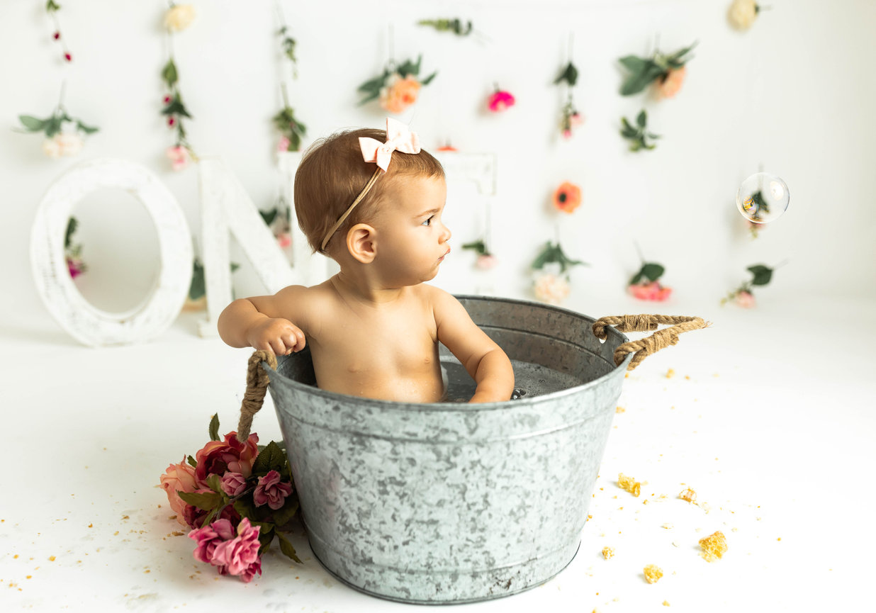 12-month-old baby posing with custom outfit and props in bucket with flowers