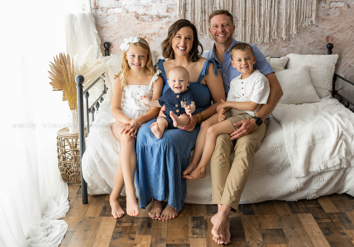 Family of five smiling in soft studio lighting with neutral bed backdrop