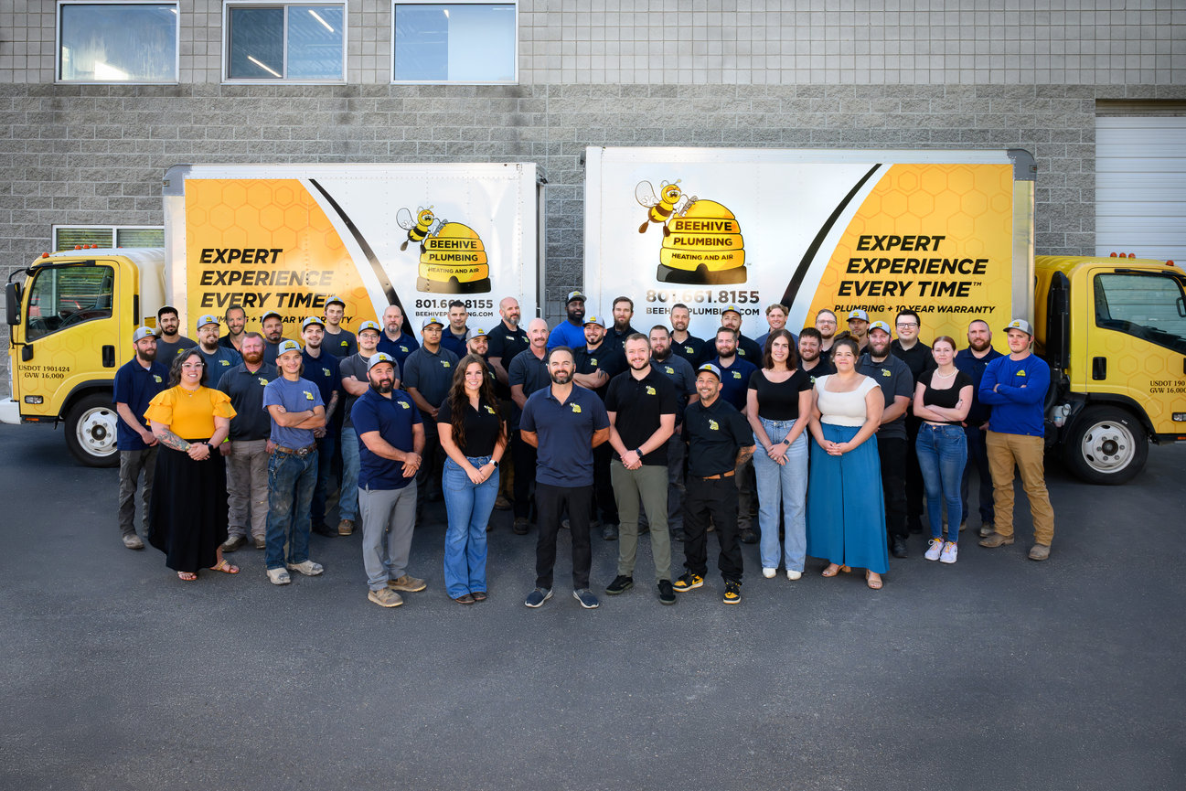 Group photo of the BeeHive Plumbing team in front of two trucks, showcasing camaraderie and professionalism.
