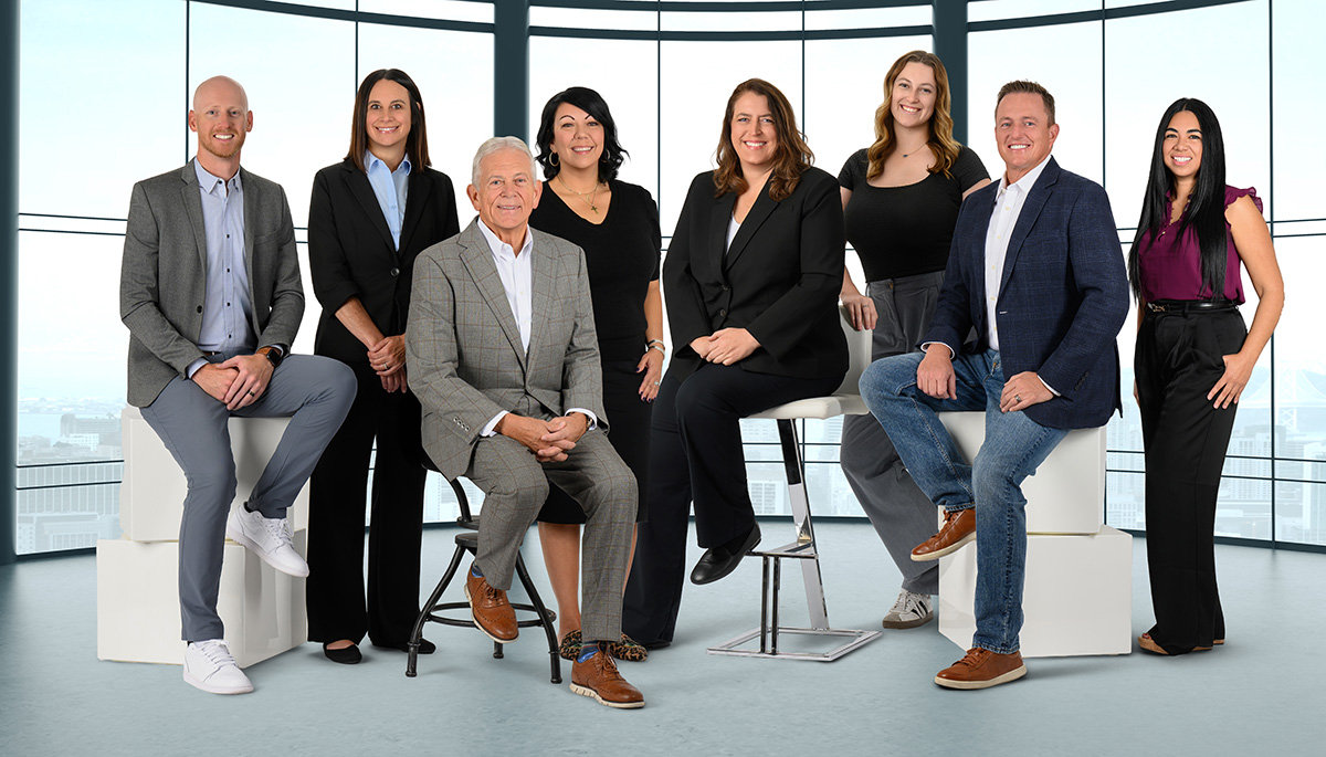 A group of six women and two men in business attire posing in a modern office setting.