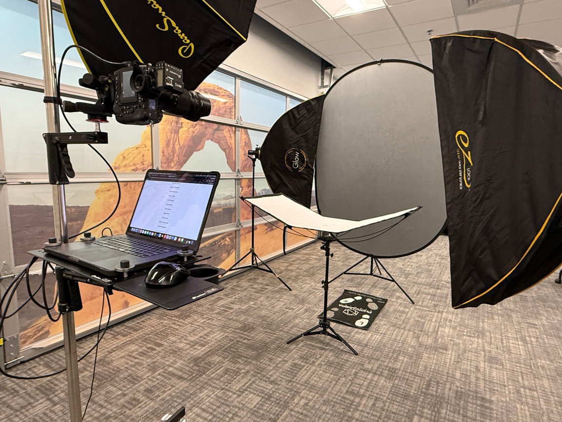 Professional photo studio setup with camera, laptop, lights, and softboxes in an office room