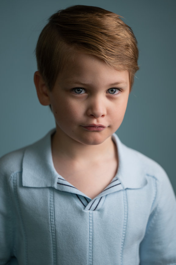 Portrait of a young boy in a light blue shirt against a muted blue background