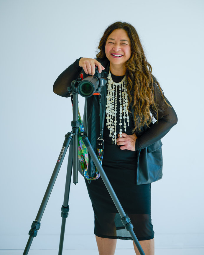 Smiling woman with camera on tripod in a studio against a white background