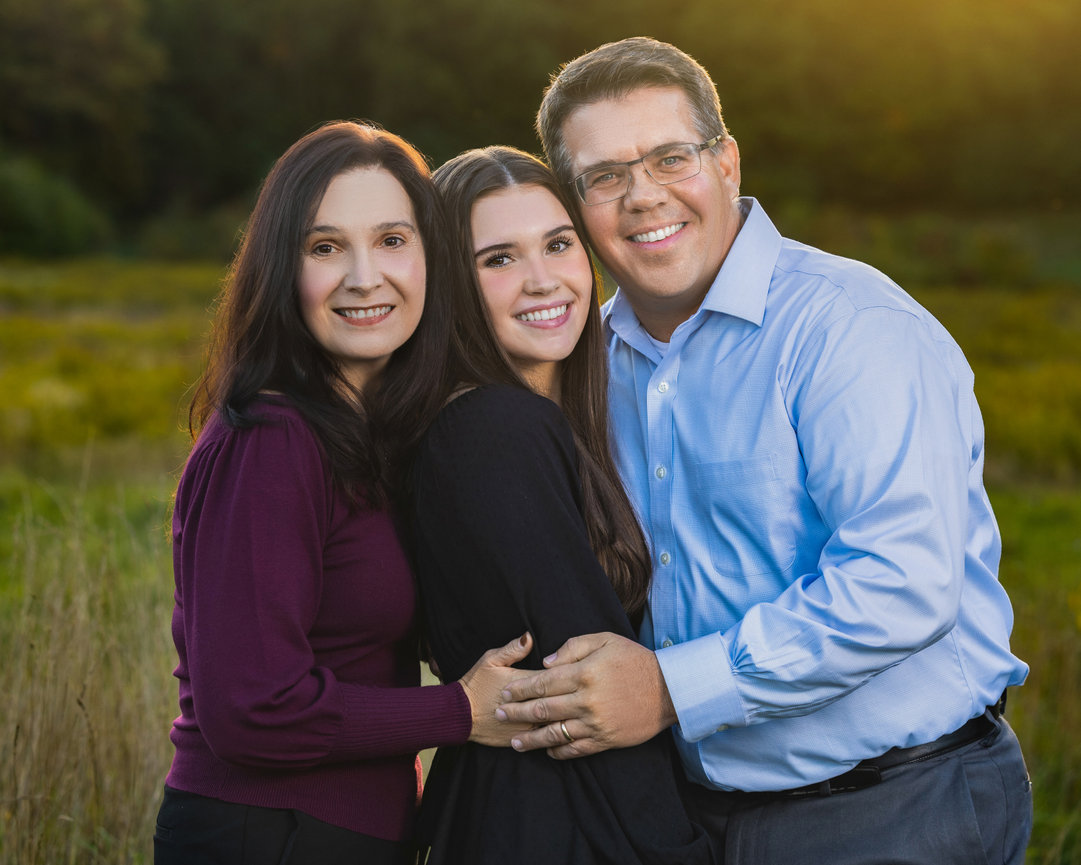 outdoor family portrait of parents with high school senior daughter in field during the fall westwood ma