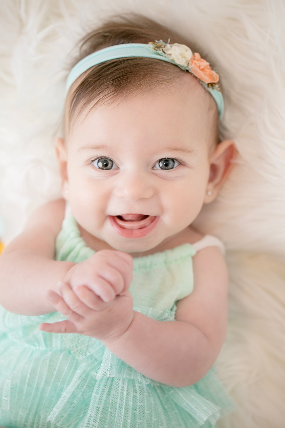 Baby smiling with hands together in a mint green dress