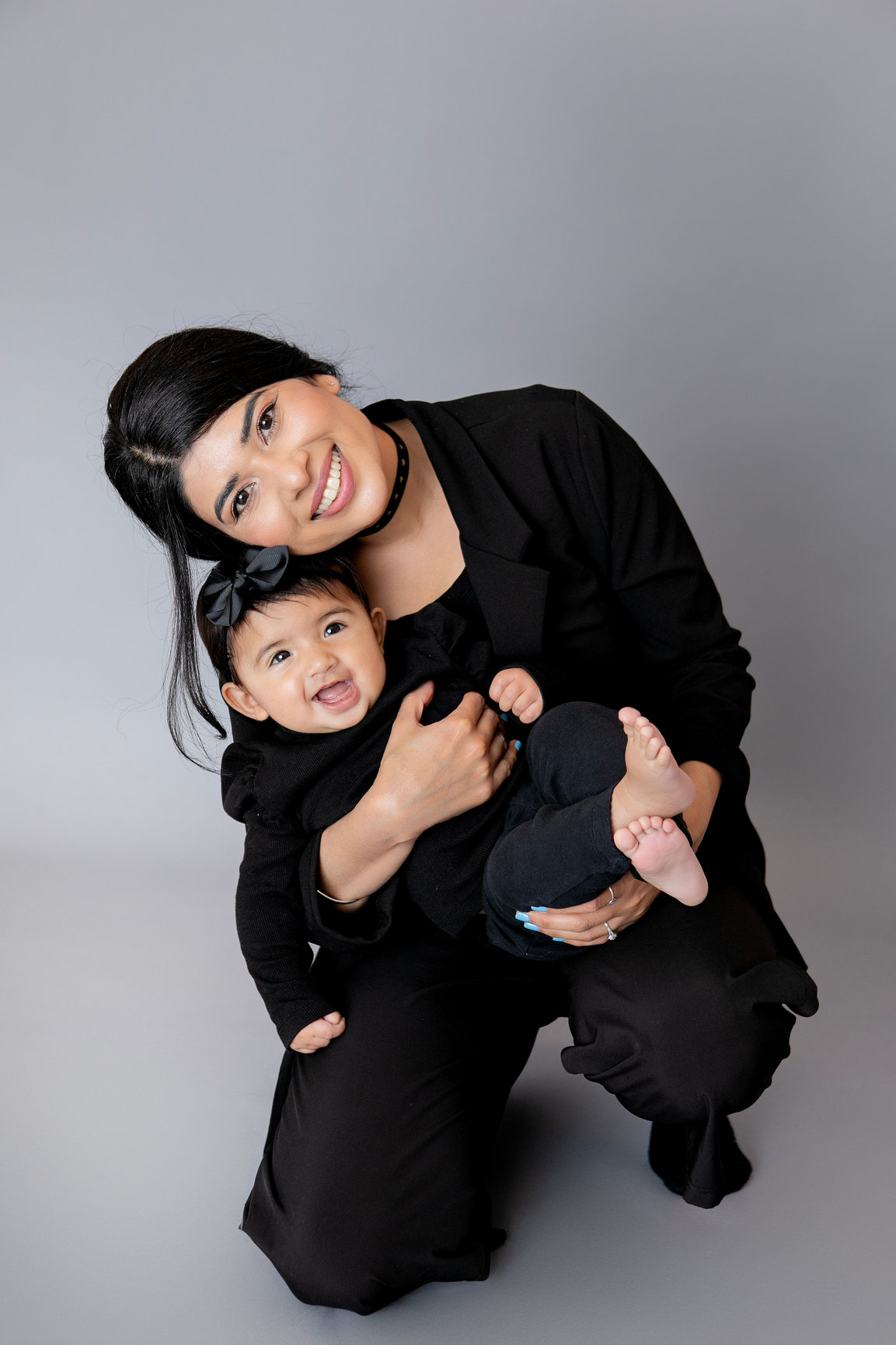 Mother cuddling her baby against a grey backdrop